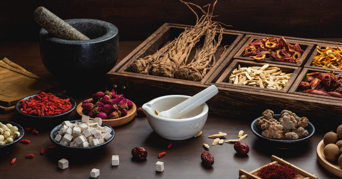 Mesa com várias ervas chinesas, incluindo raízes e flores, utilizadas na medicina tradicional.